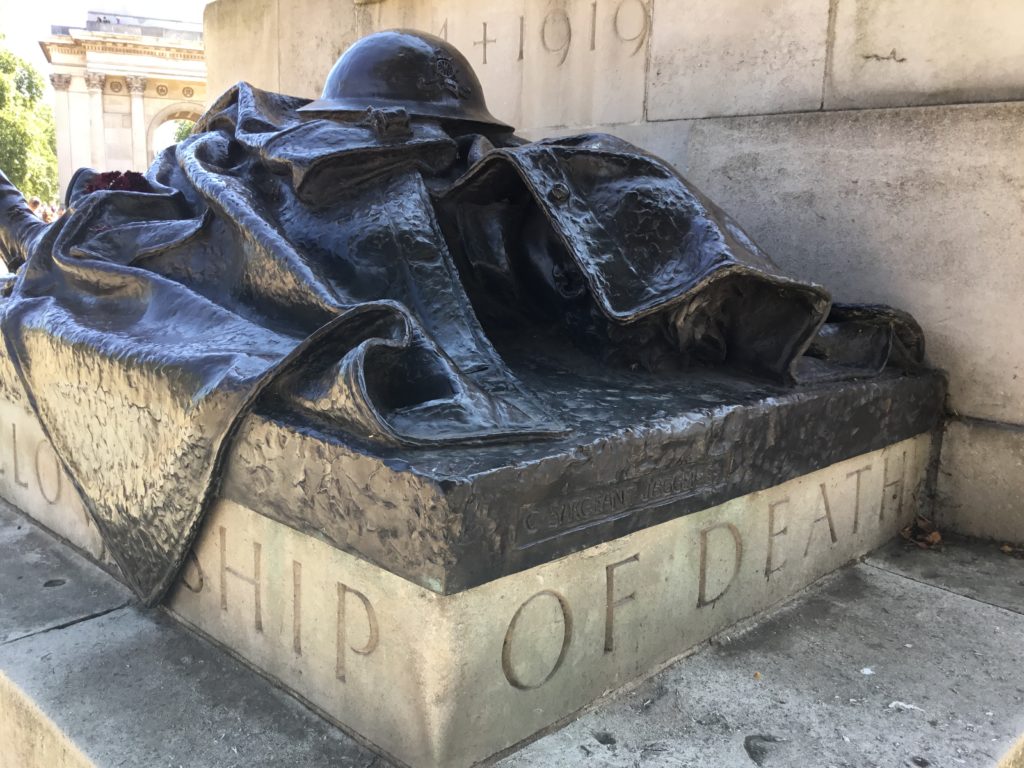 Bronze statue of a fallen soldier with great coat and helmet covering him. This one of four soldier statues at the Royal Artillery Memorial, London. Atop the memorial, but not shown, is a 9.2 Howitzer.