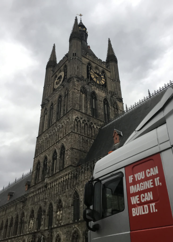 The clock tower of the Cloth Hall at Ieper (Ypres). A modern transport truck cab sits in front of the Cloth Hall. The lettering on the cab, "If you can imagine it, we can build it."