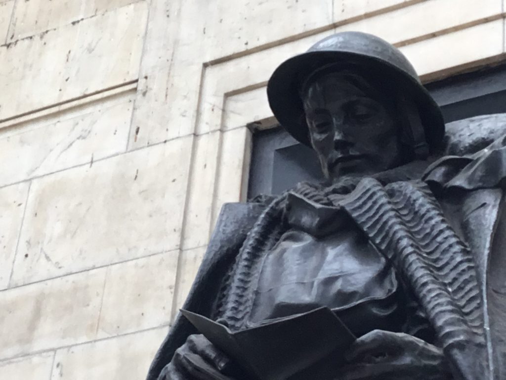 Statue of a soldier looking down at a letter. The soldier is wearing a helmet, heavy jacket known as a great coat and gas mask bag. The soldier's face appears thougthful.