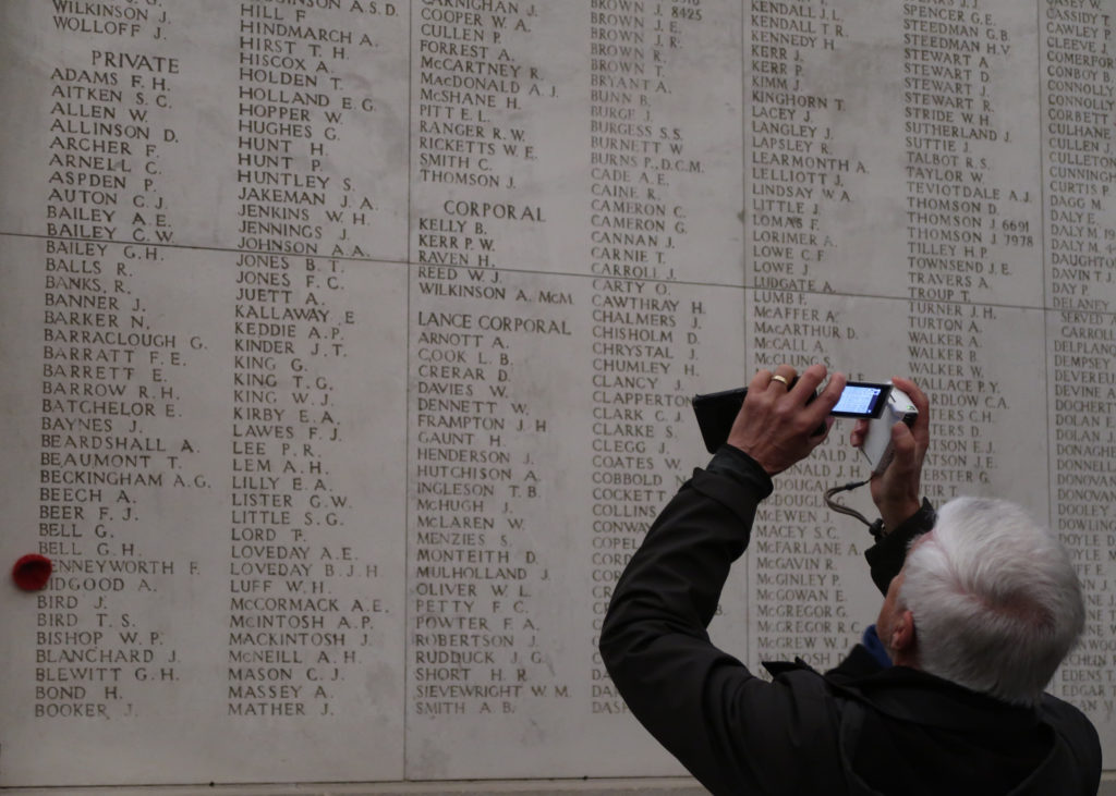An elder citizen visiting at Menin Gate raises his cell phone to take a picture of the names on the memorial.