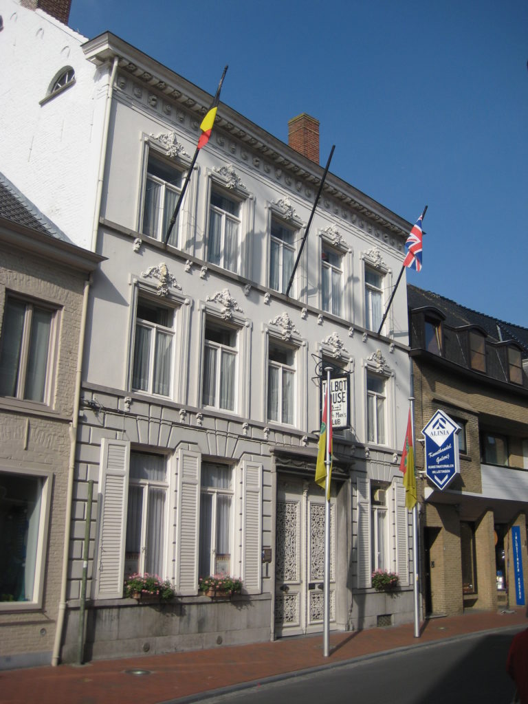 Exterior view of Talbot House, in Poperinge, Belgium. The flags of Belgium and the United Kingdom out front and above a sign lettered Talbot House.