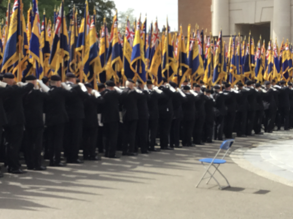 A group of British Legion veterans carrying their branch colours stands outside the Menin Gate, Ieper Ypres), Belgium. A lone chair sits along side.