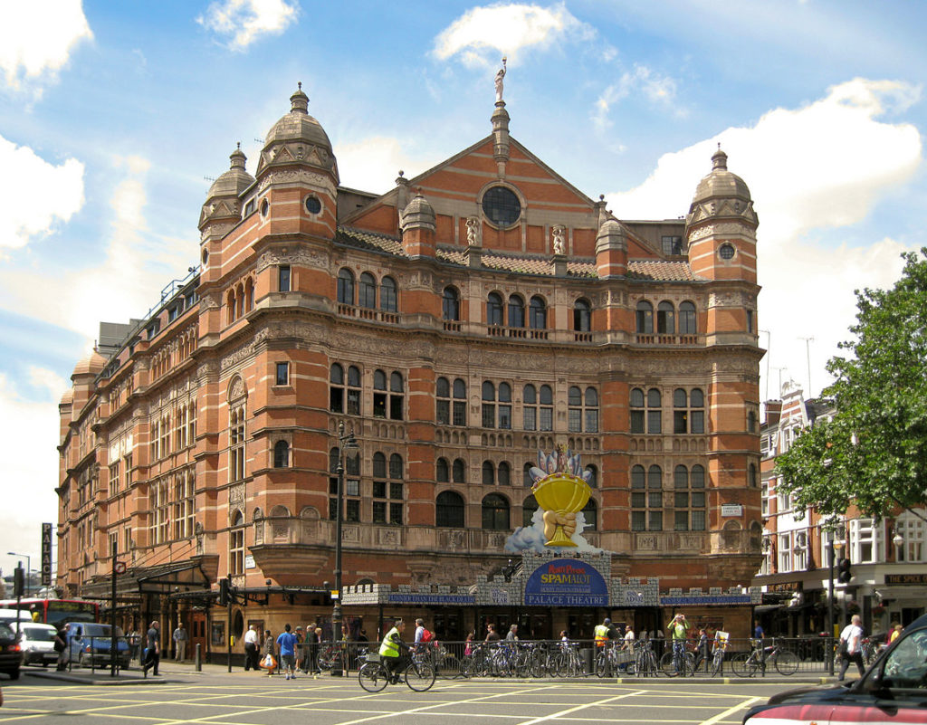 The Palace Theatre, London, England at the time. A beautiful Victorian two tone brown building with tower like structures at the corners. Multiple windows can be seen along the sides.