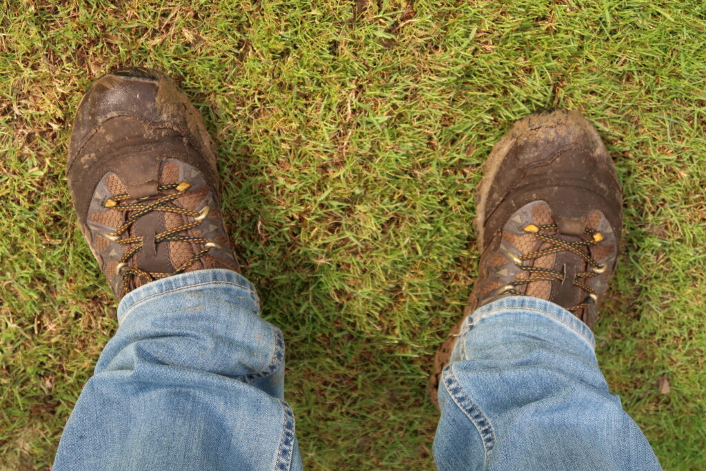 The author stands of a grassy field of the Ypres Salient, Belgium. He wears faded denims and has mud on his boots.