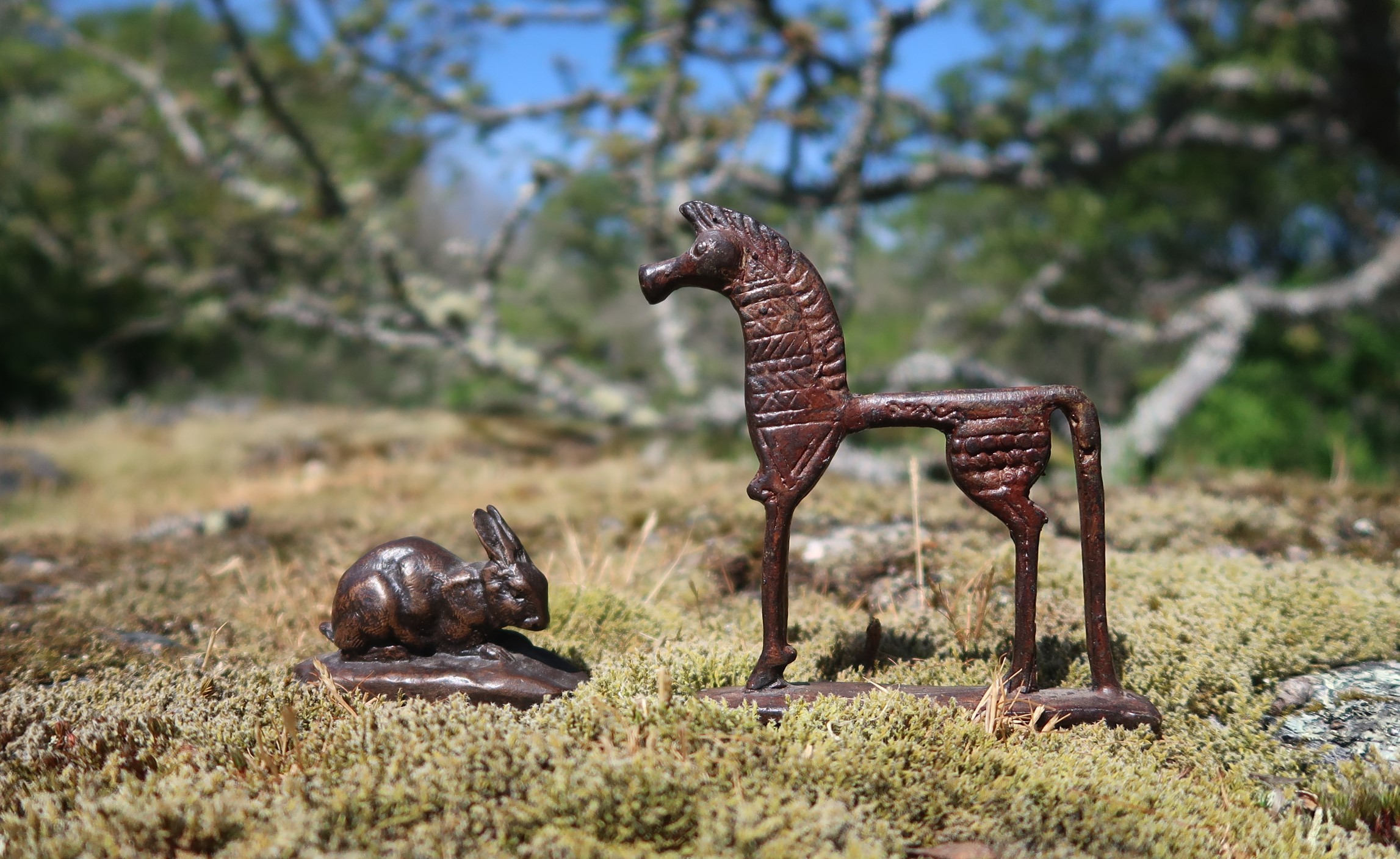 The bronze rabbit and the iron horse on a stony field. Tangles branches in the background.