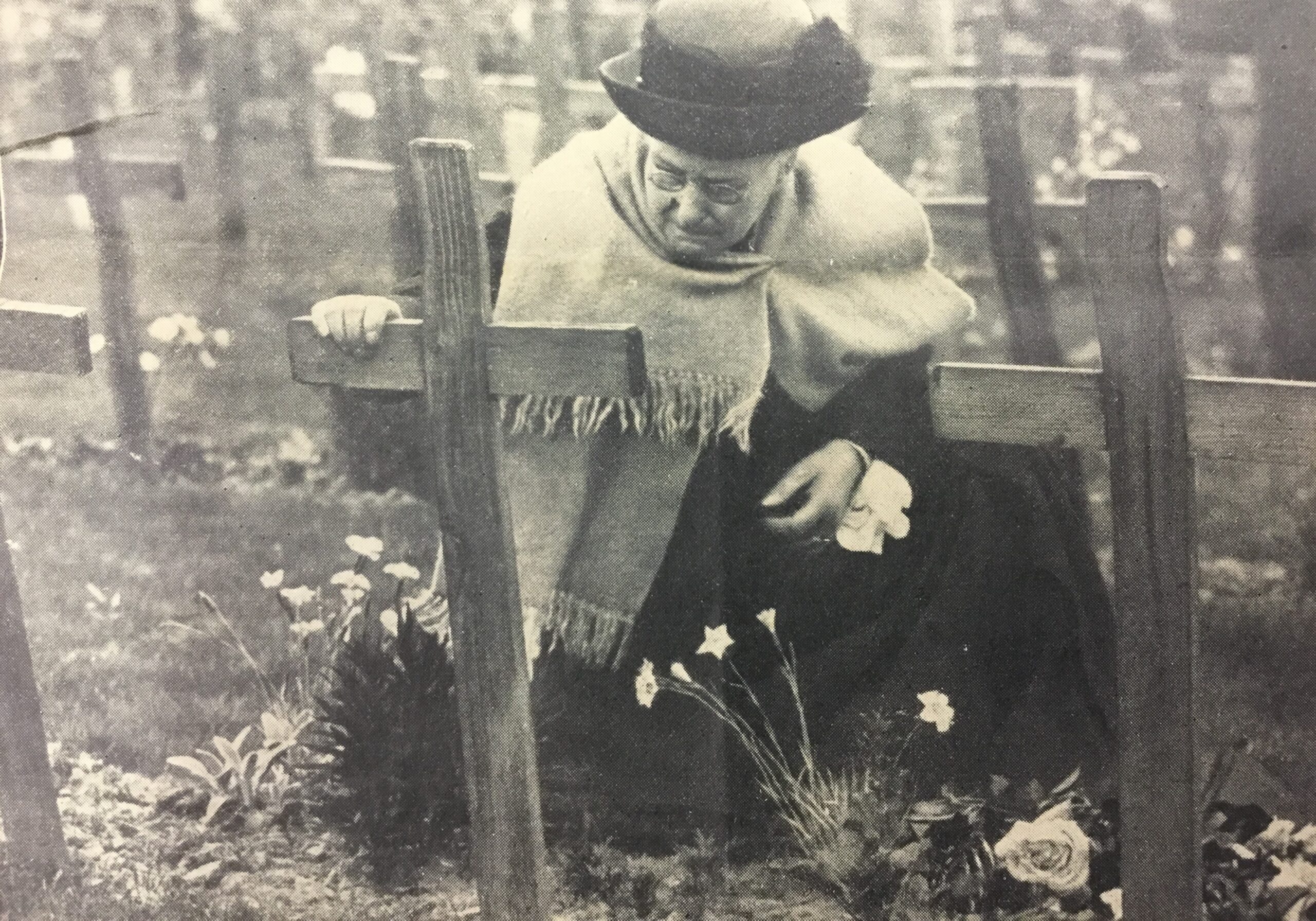 An elderly woman kneels before her son's grave.